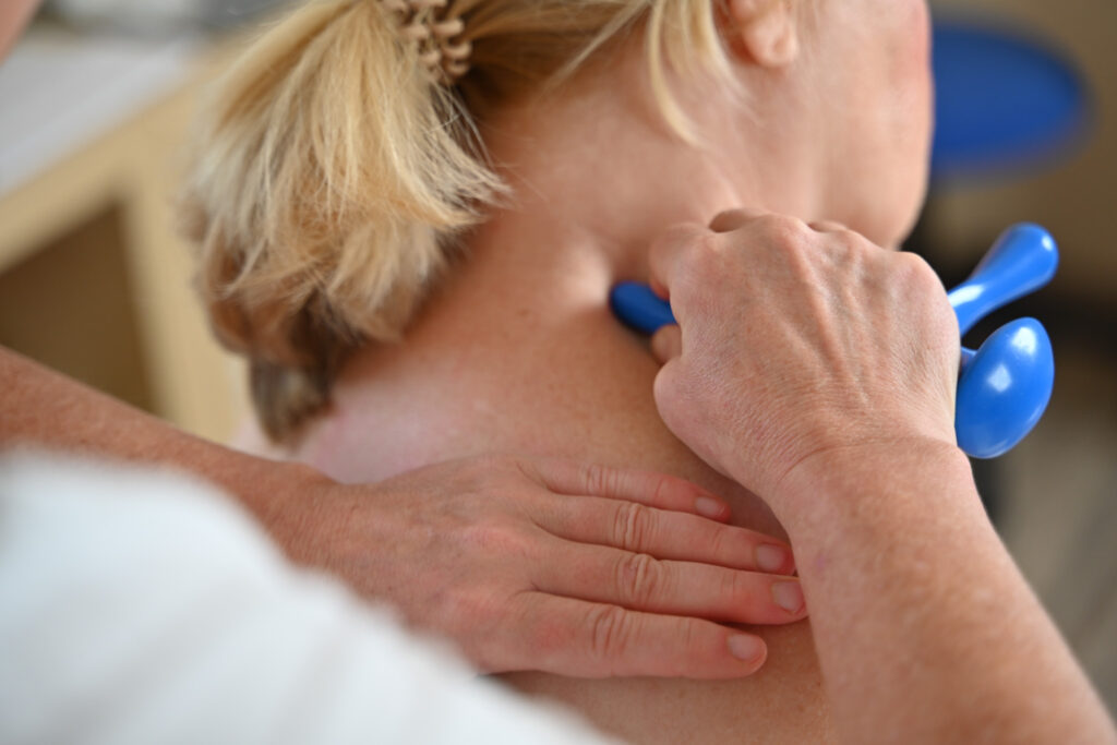 Physiotherapie. Die Therapeutin behandelt den Nacken der Patientin mit einem Handgerät um Verspannungen zu beseitigen
