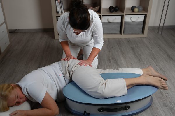 Die Patientin liegt seitlich auf dem Osflow-Therapiegerät. Die Therapeutin behandelt mit ihren Händen die Hüfte der Patientin.